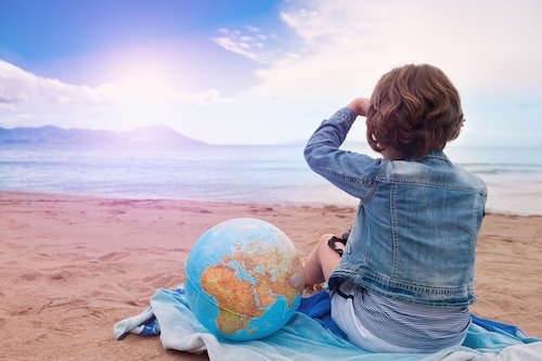 girl with globe looking across the sea - kids world travel guide